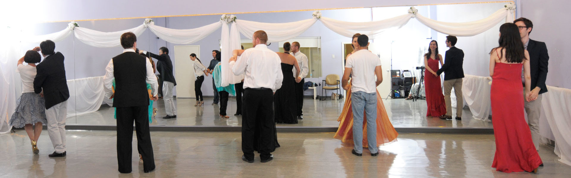 Dance couples preparing for their next steps in a ballroom setting, dressed in elegant attire, with reflections in the mirror capturing the moment.