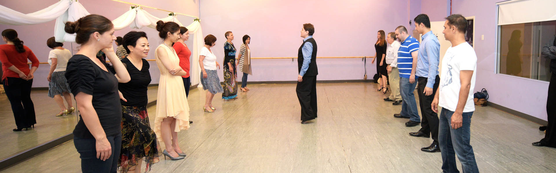 Dance class at Dancingland Dance Studio with students lined up and listening attentively as the instructor demonstrates steps.